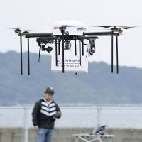 A drone lifts a package containing daily items for delivery to an island 2.5 km away during a test flight Tuesday in the city of Fukuoka. NTT Docomo Inc. is leading the project in hopes of launching a drone delivery service in fiscal 2018. | KYODO