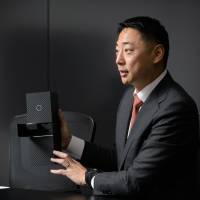 Shin Sakane, president and CEO of Seven Dreamers Laboratories Inc., speaks while holding a model of the Laundroid robot during an interview in Tokyo on Nov. 21. | BLOOMBERG