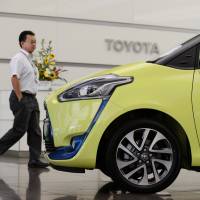 A man walks past a Toyota Sienta displayed at the company\'s head office in Tokyo. | BLOOMBERG