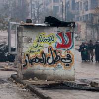 People carry their belongings as they flee deeper into the remaining rebel-held areas of Aleppo Tuesday. The Arabic words read, \"No to monopolizing commodities and raising prices under the siege.\" | REUTERS