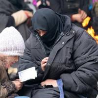 A woman sits with her child reading the Quran while waiting to be evacuated with others from a rebel-held sector of eastern Aleppo, Syria, on Saturday. | REUTERS