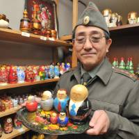 Kazuharu Iwahashi, owner of the Russian Tea specialty shop in Taito Ward, Tokyo, holds matryoshka dolls featuring past Russian leaders on Nov. 23. | YOSHIAKI MIURA