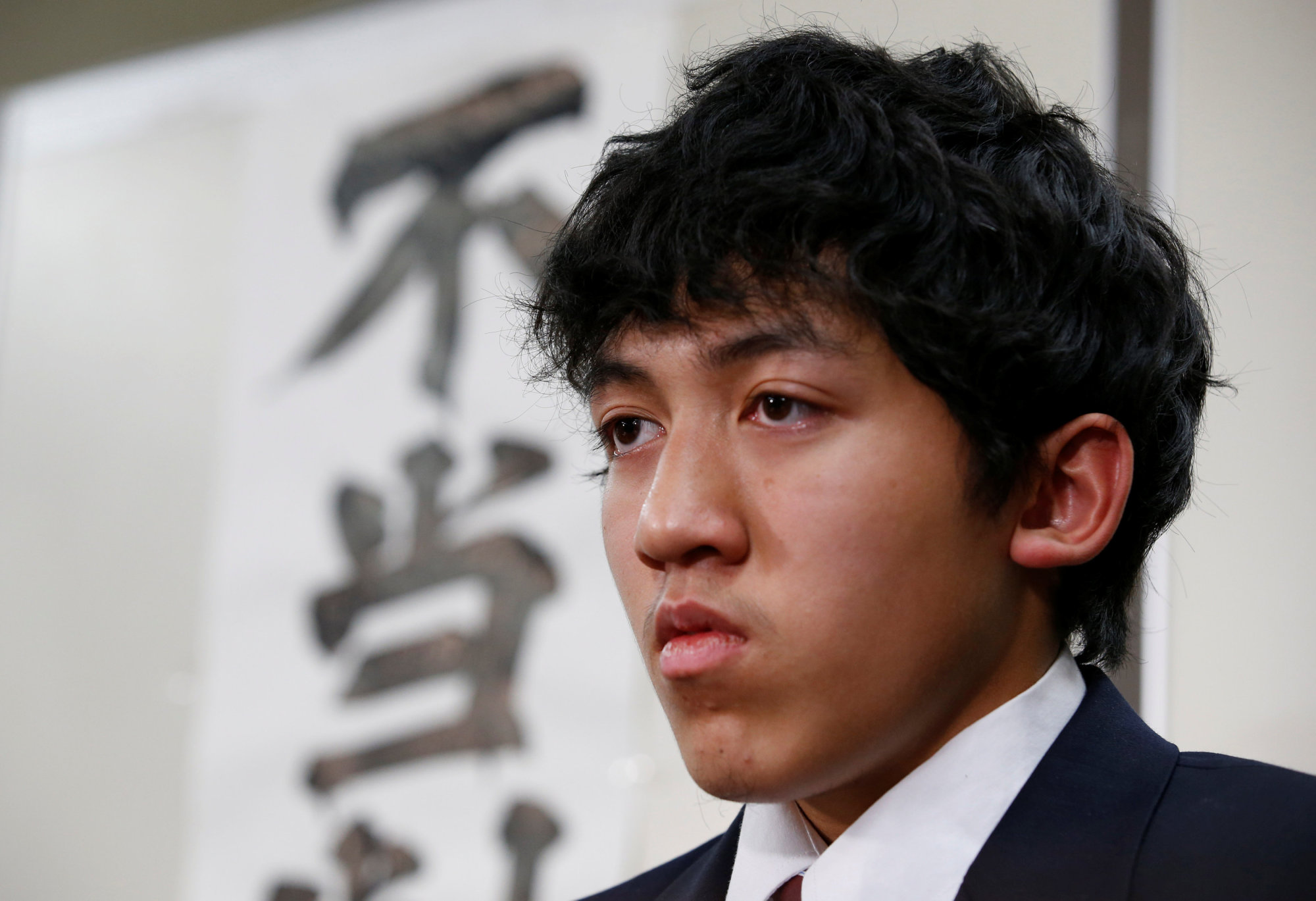 Utinan Won, a 16-year-old high school student living in Japan without a visa, attends a news conference in Tokyo on Tuesday. The characters on the wall are part of a banner that reads, 'Unjust ruling.' | REUTERS