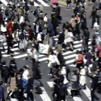 Pedestrians cross an intersection in Tokyo. The government on Tuesday unveiled a draft guideline for a system of \"equal pay for equal work\" regardless of employment status. | BLOOMBERG