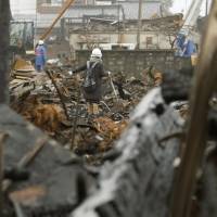 A woman carrying a shovel searches for her belongings in a fire-ravaged neighborhood of Itoigawa, Niigata Prefecture, on Saturday. | KYODO