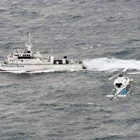 A Japan Coast Guard patrol boat and a helicopter search for the capsized Daifuku Maru and its crew off the coast of Matsue, Shimane Prefecture, on Wednesday. | KYODO