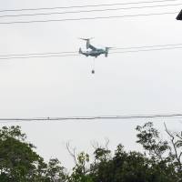 A U.S. Marine Corps MV-22 Osprey carrying an object is seen flying over the village of Ginoza in Okinawa Prefecture on Tuesday. | GINOZA MUNICIPAL GOVERNMENT/ VIA KYODO