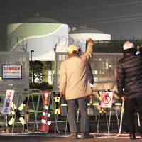 Men raise their fists in protest Thursday in front of the No. 1 reactor at the Sendai nuclear power plant in Kagoshima Prefecture, which was restarted the same day. | KYODO