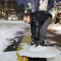 A man is seen shoveling snow on a street on Saturday evening in Sapporo. | KYODO