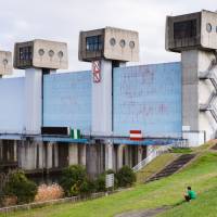 Grass and concrete: A man relaxes near the Iwabuchi Water Gate. The surrounding area is a popular space for cycling, fishing and picnics. | LANCE  HENDERSTEIN