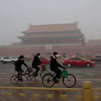 People wearing masks cycle past Tiananmen Gate after a red alert was issued for heavy air pollution in Beijing on Dec. 20. | REUTERS