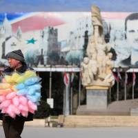 A man sells cotton candy near a banner for Syria\'s president Bashar Assad in Aleppo, Syria, Monday. | REUTERS