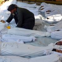 A man holds a dead child among bodies of people whom activists say were killed by nerve gas in the Damascus suburb of Ghouta in August 2013. | REUTERS