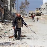 A man on crutches walks through a damaged neighborhood in Aleppo, Syria, Monday. | REUTERS