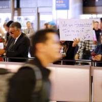 Attorney Sabra Gandhi holds up a sign while travelers pass by amid protests over President Donald Trump\'s executive order banning travel from seven Muslim-majority countries continue at Los Angeles International Airport Sunday. | AP