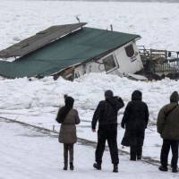 People walk past a houseboat trapped in the frozen Danube River, in Belgrade Tuesday. | REUTERS
