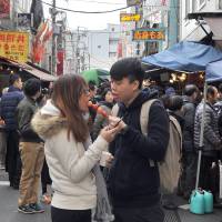 A couple share a strawberry skewer bought at the Tsukiji fish market, which sells not only seafood but also snacks and desserts. | YOSHIAKI MIURA