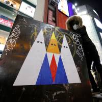 A graffiti artist known as 281_Anti Nuke poses for a photo next to an example of his recent artwork depicting U.S. President Donald Trump, in Tokyo\'s Shibuya district on Friday. | REUTERS