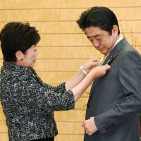 Tokyo Gov. Yuriko Koike attaches a 2020 Tokyo Olympics and Paralympics badge to the jacket of Prime Minister Shinzo Abe before their meeting at his office in Tokyo on Tuesday. | KYODO