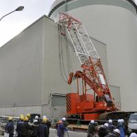 Workers on Saturday examine a crane that collapsed onto a building that houses spent nuclear fuel at the Takahama nuclear power plant in Fukui Prefecture. | KYODO