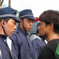 A still photograph from the documentary \"Takae &#8212; Mori ga Naiteiru\" depicts clashes between riot police and local residents opposing construction of U.S. helipads near a U.S. military training site in Takae, Okinawa, in July. | &#169;MORINOEIGASHA