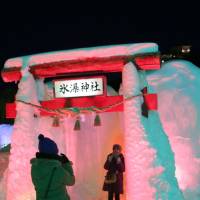 People photograph an ice sculpture portraying a shrine gate at a festival Wednesday in Kamikawa, Hokkaido. The event features around 30 colorfully lighted works and will run through March 20. | KYODO