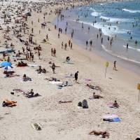 Beachgoers relax on Sydney\'s Bondi Beach on February on Saturday. Thousands of people flocked to Sydney\'s beaches to cool off, prompting warnings from lifeguards to stay close to shore and take precautions against the sun. | AFP-JIJI