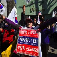 Pro-government activists shout and wave the national flag outside the Constitutional Court in Seoul on Monday. | AFP-JIJI