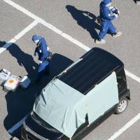 Police officers investigate a car in which a suspect who shot two men and fled the scene killed himself Wednesday in Kamisu, Ibaraki Prefecture. | KYODO