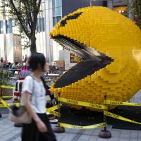 A woman walks past a giant Pac-Man in Tokyo\'s Shinjuku area installed in 2015 to promote the movie \"Pixels.\" Masaya Nakamura, the \"Father of Pac-Man\" who founded the Japanese video game company behind the hit creature-gobbling game, died on Jan. 22. | AP