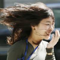 A woman\'s hair flies around her head in Tokyo\'s Marunouchi business district on Friday as Japan\'s first spring gale, known as haru-ichiban, blew through the Kanto region. | KYODO
