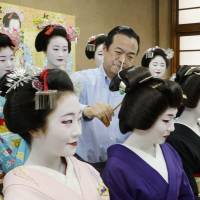A stylist checks the hair of a maiko (apprentice geisha) in the Gion district of Kyoto on Wednesday during a photo session for brochures advertising the annual \"Miyako Odori\" dance performances on April 1-23. | KYODO