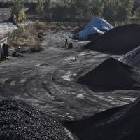A man walks past piles of coal at a port in Qinhuangdao, China, on Oct. 28, 2016. | BLOOMBERG
