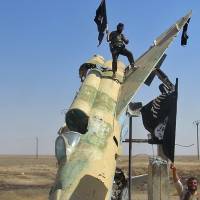 Islamic State fighters wave the group\'s flag from a damaged government fighter jet following the battle for the Tabqa air base, in Raqqa, Syria, in this undated photo posted to the internet in August 2014. | AP