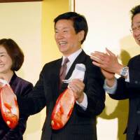 Chiba Gov. Kensaku Morita holds a pair of red fish to celebrate his election victory in the city of Chiba on Sunday evening after voters gave him a third term. | KYODO