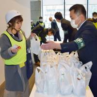 Participants receive a supply of emergency food at the Cabinet Office building during a disaster drill in central Tokyo on Monday. | KYODO