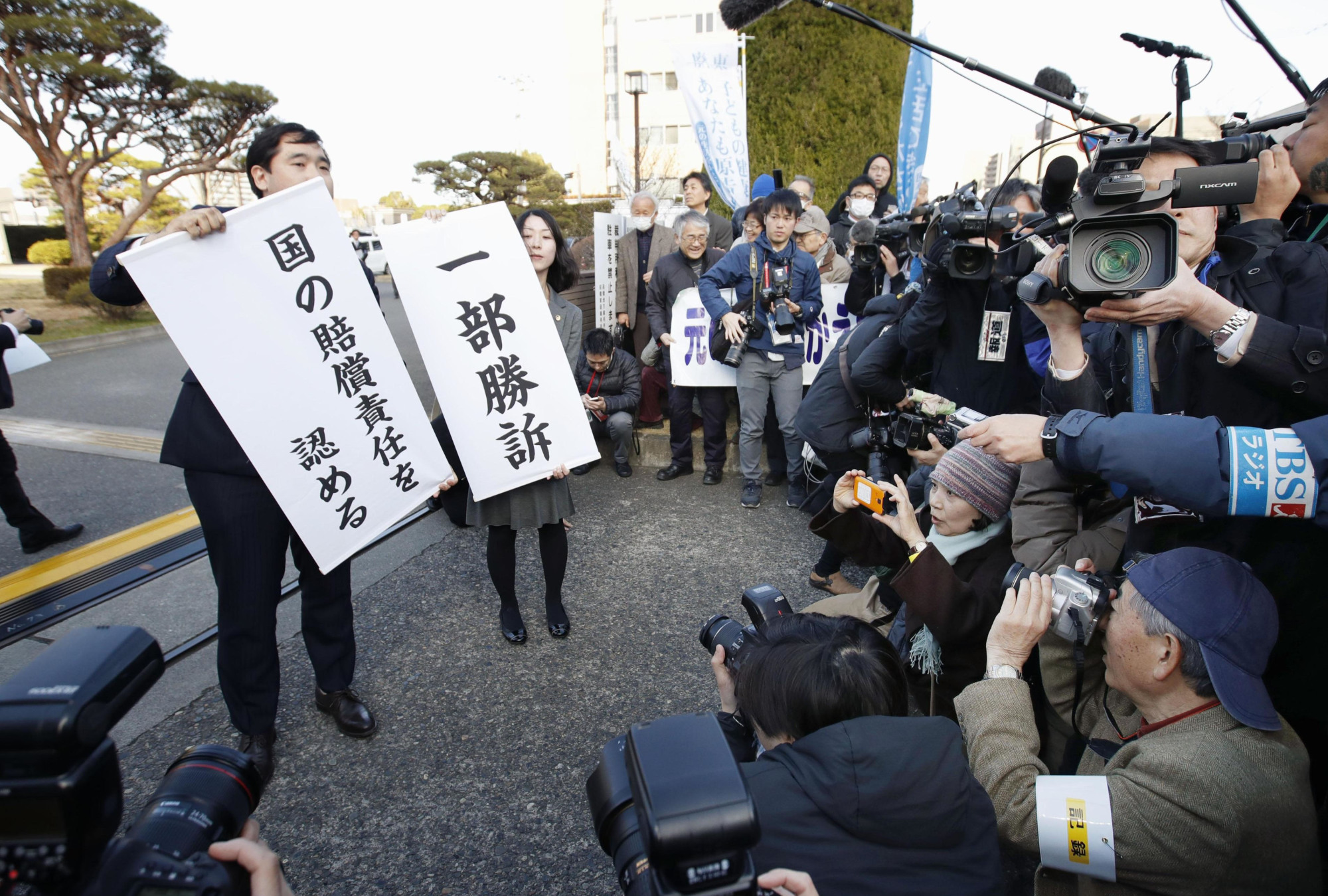 Supporters of plaintiffs seeking compensation for Fukushima evacuees unfurl banners in front of the Maebashi District Court in Gunma Prefecture announcing the court's decision Friday. | KYODO