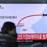 A woman walks in front of a TV screen at Seoul Train Station showing a news program reporting on North Korea\'s firing of four missiles Monday. | AP
