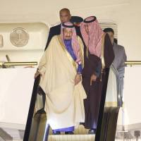 Saudi Arabian King Salman bin Abdul-Aziz (left) rides on a special escalator as he disembarks from his plane following its arrival at Haneda airport in Tokyo on Sunday evening. Salman\'s visit to Japan is part of the monarch\'s month-long tour of Asia. | AP