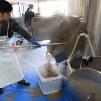 An employee of Kyoto Brewing Co. removes spent grain from the brew tank. | SATOKO KAWASAKI