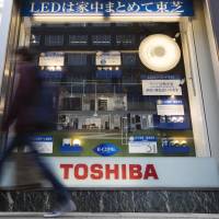 A pedestrian walks past a Tokyo store displaying Toshiba Corp. products in December 2015. Public-private consortium mulled to bid for Toshiba's chip unit as security concerns mount