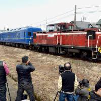 A diesel-powered express train runs in Akita Prefecture in April last year as railroad buffs standing beside the tracks take photographs. | KYODO
