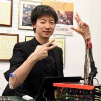 Meltin MMI Co. CEO Masahiro Kasuya poses with a robotic hand the firm has developed that picks up electric signals from muscles and replicates human hand movements. | SATOKO KAWASAKI