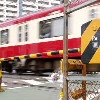 Flowers are placed at a train crossing Sunday to pray for two men who were fatally struck by a train at Hatcho-nawate Station on the Keikyu Line in Kawasaki Saturday. | KYODO