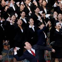 Japan Airlines Co. President Yoshiharu Ueki prepares to throw a paper plane as he joins newly hired JAL group employees at a welcome ceremony in a hangar at Tokyo\'s Haneda airport on Monday. About 890,000 new recruits marked their first day at work the same day at companies, public offices and other organizations across the country. | REUTERS