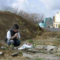 A man prays at the site where the house of a former colleague used to stand in the village of Minamiaso, Kumamoto Prefecture, on Sunday. The magnitude-7.3 quake that hit the prefecture a year ago destroyed the property, killing his colleague. | KYODO