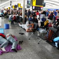 People sleep next to their luggage at Heathrow Terminal 5 in London Sunday. Heathrow chaos continues as British Airways scrambles to recover from IT crash