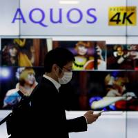 A man using his mobile phone walks past Sharp Corp\'s liquid crystal display monitors showing the company\'s Aquos television in Tokyo on March 30, 2016. | REUTERS