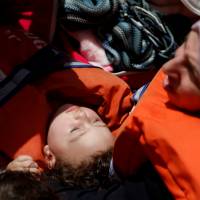 A child migrant lies in its mother\'s lap on a rigid-hulled-inflatable-boat (RHIB) alongside the Malta-based NGO Migrant Offshore Aid Station (MOAS) ship Phoenix during a rescue operation in the central Mediterranean, in international waters off the Libyan coastal town of Sabratha May 4. | REUTERS