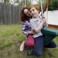 In this Thursday photo Susan Grenon plays with her son, Pauly, in the backyard of their home in Smithfield, Rhode Island. Guenon makes sure her son is lathered with sunscreen before he leaves for school in the morning, but the red-headed 10-year-old can’t bring a bottle to reapply it without a doctor’s note. More states letting kids bring sunscreen to school without doctor's OK